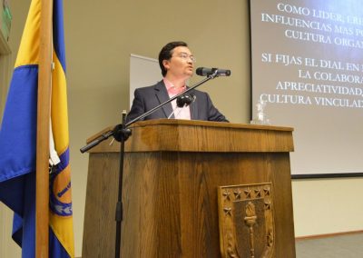 Expositor en el podio en primer plano y bandera UdeC